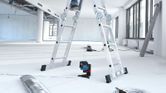 Laser leveling tool projecting red lines on a floor beneath a person on a ladder.