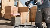 A person wearing safety equipment mixes mortar in a bucket with a stirring tool.