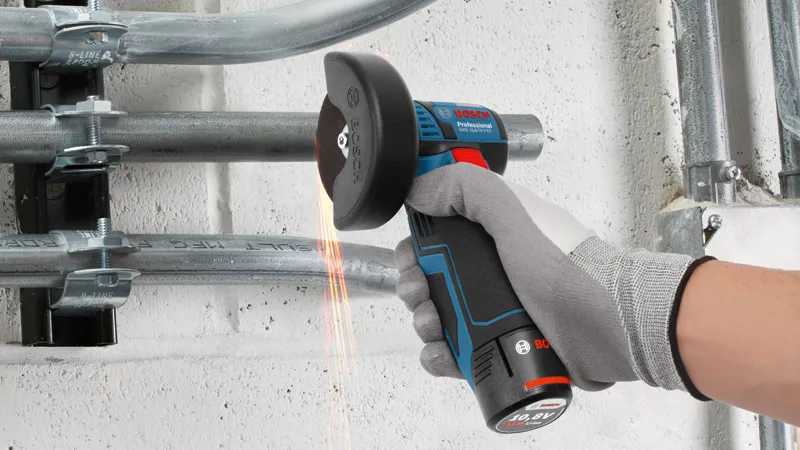 GWS 12V-76 A person wearing safety equipment cuts metal conduit with a cordless angle grinder.