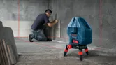 A person installs wall tiles using a laser leveling tool for alignment.
