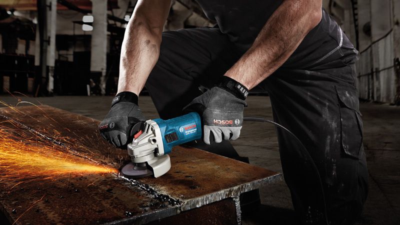 A person wearing safety equipment grinds metal, producing sparks on a workbench.