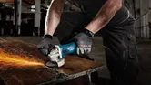 A person wearing safety equipment grinds metal, producing sparks on a workbench.