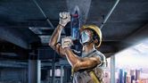 A person wearing safety equipment drills into a concrete ceiling at a construction site.