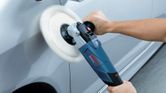 A person uses a polisher to buff the surface of a car door.