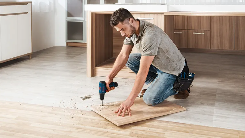 GSR 120-LI A person drills into a wooden board on the floor in a kitchen under renovation.