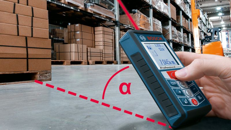 A person uses a laser measure to check distance in a warehouse with stacked boxes.