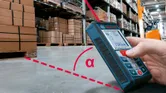 A person uses a laser measure to calculate distance on a warehouse floor.