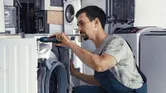 A person repairs a washing machine with a cordless screwdriver.