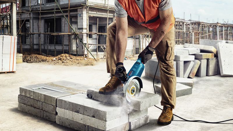 GWS 2200 A person wearing safety equipment uses a power cutter to cut concrete blocks on a construction site.