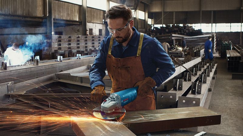 GWS 2200 A person wearing safety equipment grinds metal, producing sparks in a factory.