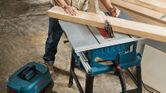 A person wearing safety equipment cuts wood with a table saw in a workshop.
