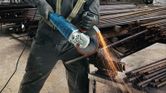 A person wearing safety equipment cuts rebar with a large angle grinder, sparks flying.
