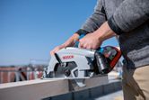 Person using a cordless circular saw to cut a wooden beam outdoors.