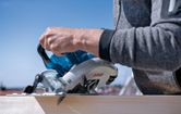 A person cuts wood outdoors with a cordless circular saw.