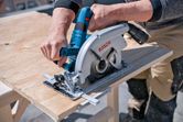 A person cuts plywood with a cordless circular saw on a workbench.