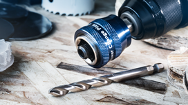 Metal drill bit and quick-change drill chuck resting on a wooden surface.