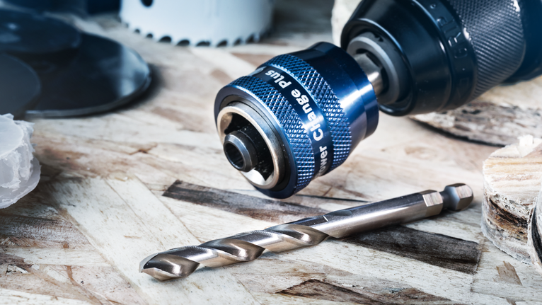 Metal drill bit and quick-change drill chuck resting on a wooden surface.