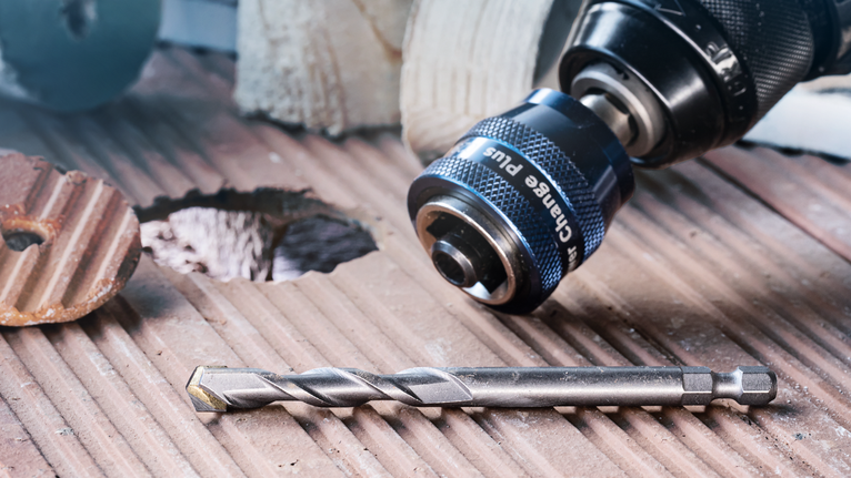 Drill with quick-change chuck and masonry bit on a tiled surface next to a drilled hole.