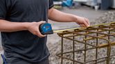 A person uses a tape measure to check the width of a metal rebar structure.