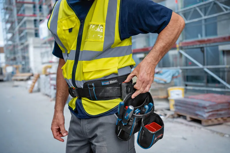 GWT 4 Person wearing safety equipment adjusts a tool belt at a construction site.