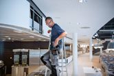 A person wearing safety equipment stands on a ladder installing a ventilation system.