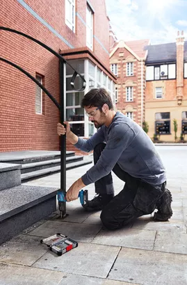 Professional Promotion Set of Combo GDX 18V-285 + GSB 185-LI with 2x2.0Ah, GAL 18V-20 in Case A person wearing safety equipment drills into stone steps, installing a metal handrail.