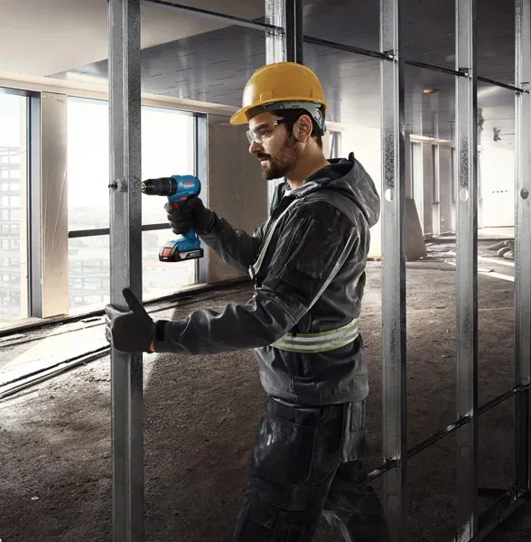 GDS 18V-350 + GSB 185 Combo A person wearing safety equipment drills into a metal stud in a building under construction.