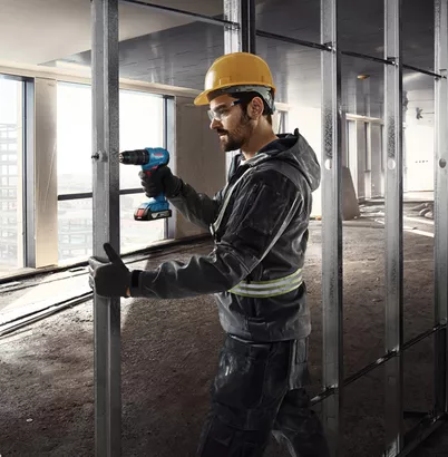 Professional Promotion Set of Combo GDX 18V-285 + GSB 185-LI with 2x2.0Ah, GAL 18V-20 in Case A person wearing safety equipment drills into a metal stud in a building under construction.