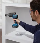 A person wearing safety equipment uses a cordless drill to install a cabinet rail.