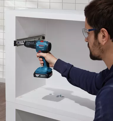 Professional Promotion Set of Combo GDX 18V-285 + GSB 185-LI with 2x2.0Ah, GAL 18V-20 in Case A person wearing safety equipment uses a cordless drill to install a cabinet rail.