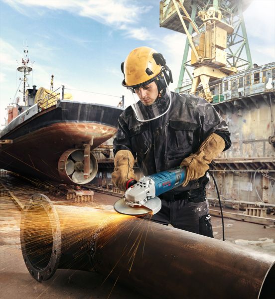 GWS 30-180 B A person wearing safety equipment grinds a large metal pipe at a shipyard.