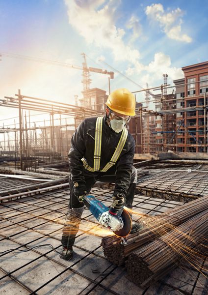 GWS 30-180 B A person wearing safety equipment uses an angle grinder to cut steel rods at a construction site.