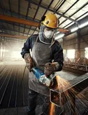 A person wearing safety equipment grinds metal, producing bright sparks in a factory.