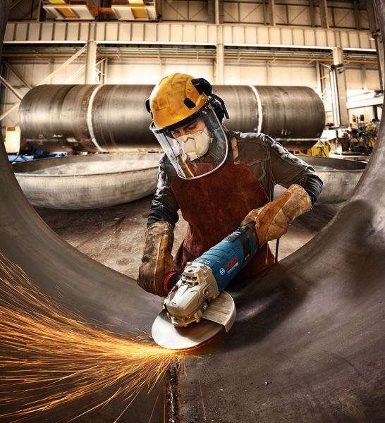 GWS 30-180 B A person wearing safety equipment grinds a large metal pipe with sparks flying.