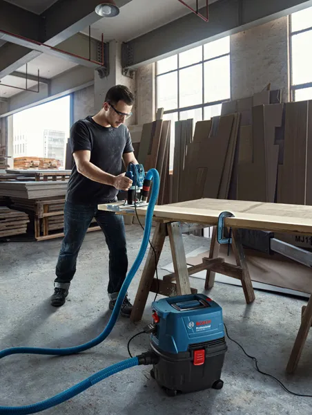 GAS 15 A person uses a wet dry extractor connected to a power tool while working on wood.
