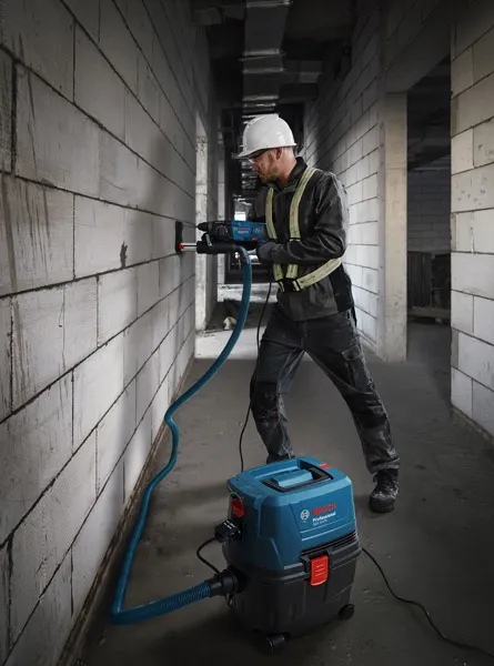 GAS 15 A person wearing safety equipment drills into a wall using a wet dry extractor.