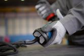 A person wearing safety equipment holds a corded power tool on a workbench.