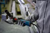 A person wearing safety equipment holds an angle grinder in a workshop.