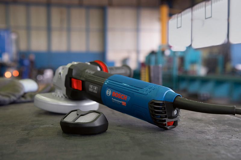 Electric angle grinder with a dust filter attachment resting on a workbench in a workshop.