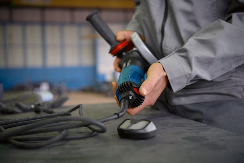 Person wearing safety equipment connects a power tool on a workbench.