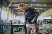A person wearing safety equipment grinds metal on a workbench, producing sparks.