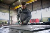 A person wearing safety equipment grinds a metal surface, creating sparks in a workshop.