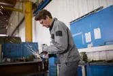 A person wearing safety equipment grinds metal, producing sparks in a workshop.