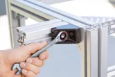 A person tightens a bolt on a metal frame with a combination wrench.