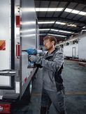 A person wearing safety equipment uses a cordless rivet gun on a truck door.