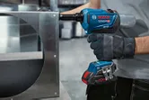 A person wearing safety equipment uses a cordless rivet gun on a metal frame.