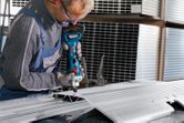 A person wearing safety equipment grinds a metal sheet with a cordless straight grinder.