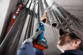 A person wearing safety equipment grinds inside a metal pipe with a cordless straight grinder.