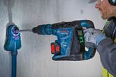 A person wearing safety equipment drills into concrete using a rotary hammer with dust extractor.