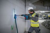 Person wearing safety equipment drills into a concrete wall using a cordless rotary hammer.